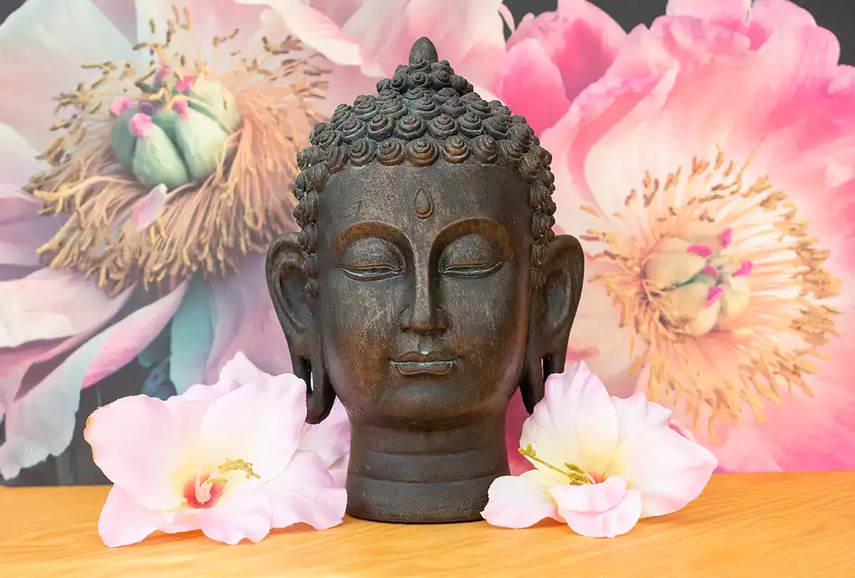 Meditieren: Wirkung auf Körper und Geist – Buddha Kopf mit Blüten im Hintergrund