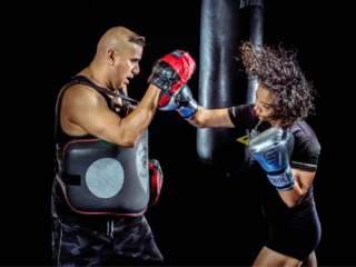 Boxen lernen - Frau trainiert mit Trainer und schlägt auf Pratzen