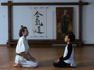 Zwei Karateka knieen voreinander. im Hintergrund sieht man Karate-Schriftzeichen