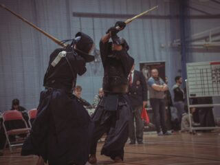 Kendo Shinai Kampftraining in einer Sporthalle - 2 Kendoka Kämpfer erheben ihre Shinais