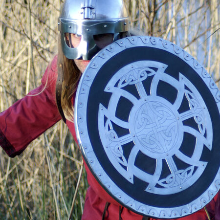 ULFBERTH Wikinger Rundschild, Schaukampftauglich (Holz, Stahl, Leder) 54,5 cm Durchmesser - eine Wikingerkrieger steht mit Schild und Helm am Schilf an einem See
