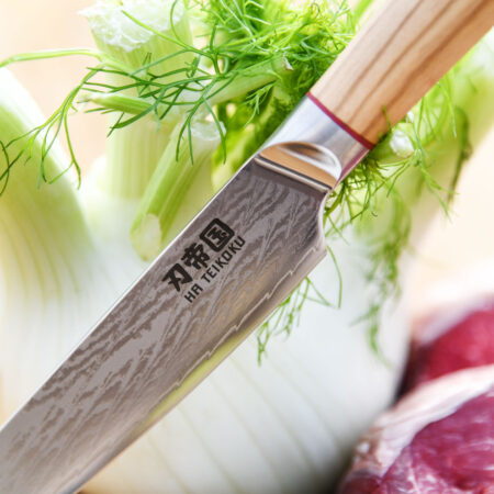 Ha Teikoku Allzweckmesser Damaststahl Olivenholz Griff - Nahaufnahme Messer lehnt an Fenchel, auf einem Holzbrett, mit frischen Kräutern, Knoblauch und einem Rindersteak