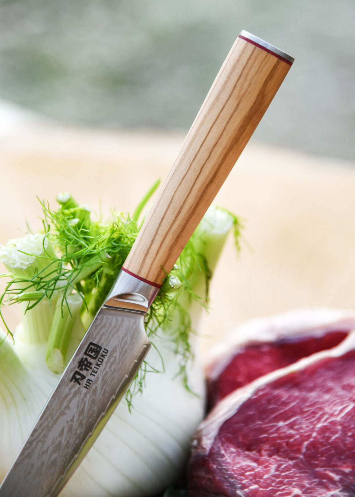 Ha Teikoku Allzweckmesser Damaststahl Olivenholz Griff - Nahaufnahme Messer lehnt an Fenchel, auf einem Holzbrett, mit einem Rindersteak