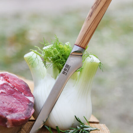 Ha Teikoku Ausbeinmesser, Damaststahl, Olivenholz - Messer lehnt an ein Fenchel an, auf einer Holzscheibe mit einem Rindersteak und Kräutern