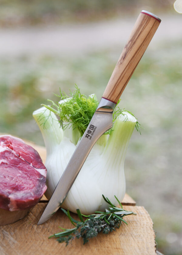 Ha Teikoku Ausbeinmesser, Damaststahl, Olivenholz - Messer lehnt an ein Fenchel an, auf einer Holzscheibe mit einem Rindersteak und Kräutern