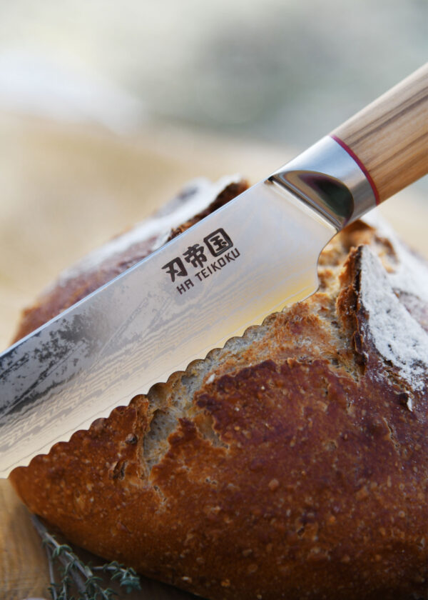Ha Teikoku Brotmesser Damaststahl Olivenholz - Nahaufnahme Klinge lehnt an Brotlaib an
