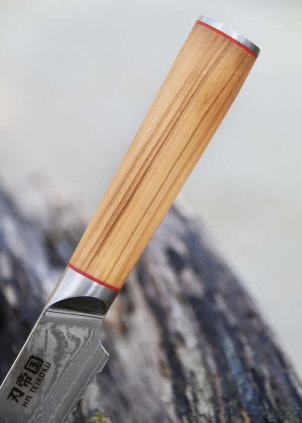 Ha Teikoku Brotmesser Damaststahl Olivenholz - Nahaufnahme Griff, teil der Klinge lehnt an ein altes graues Stück Holz