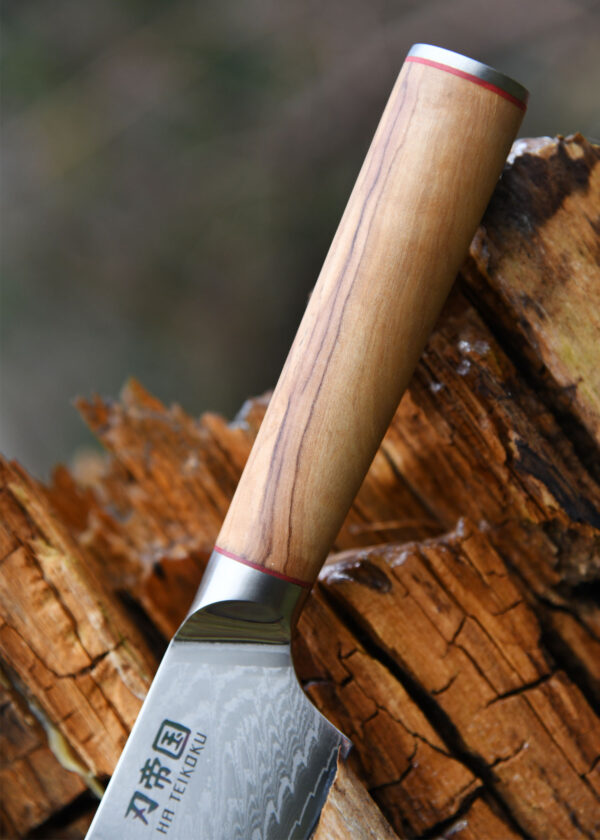 Ha Teikoku Kochmesser 16,5 cm Klingenlänge Damaststahl - Nahaufnahme Messer liegt auf einem nassen Holzscheidt, der Hintergrund verschwommen