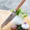 Ha Teikoku Kochmesser, 20 cm Klingenlänge, Damaststahl Olivenholz - Messer lehnt an einem Fenchel, auf einem Holzbrett mit frischem Knoblauch, Kräutern und einer Kartoffel