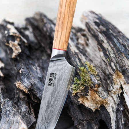 Ha Teikoku Kochmesser, 20 cm Klingenlänge, Damaststahl Olivenholz - Messer lehnt an ein altes graues Holzstück, auf einem Holztisch