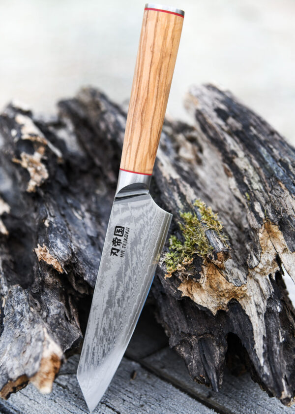 Ha Teikoku Kochmesser, 20 cm Klingenlänge, Damaststahl Olivenholz - Messer lehnt an ein altes graues Holzstück, auf einem Holztisch