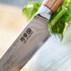 Ha Teikoku Kochmesser, 20 cm Klingenlänge, Damaststahl Olivenholz - Klinge lehnt an einem Fenchel, auf einem Holzbrett