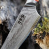 Ha Teikoku Kochmesser, 20 cm Klingenlänge, Damaststahl Olivenholz - Nahaufnahme Klinge und Griff lehnt an ein altes graues Holzstück, auf einem Holztisch