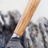Ha Teikoku Kochmesser, 20 cm Klingenlänge, Damaststahl Olivenholz - Nahaufnahme Griff und Klinge lehnt an ein altes graues Holzstück, auf einem Holztisch