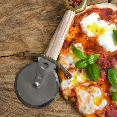 Battle Merchant Pizzaschneider Pizzaroller Templer Schwert Edelstahl, Eschenholz, Messing, Emaille - liegt auf einer Holzscheibe mit einer Pizza Mozarella mit Basilikum