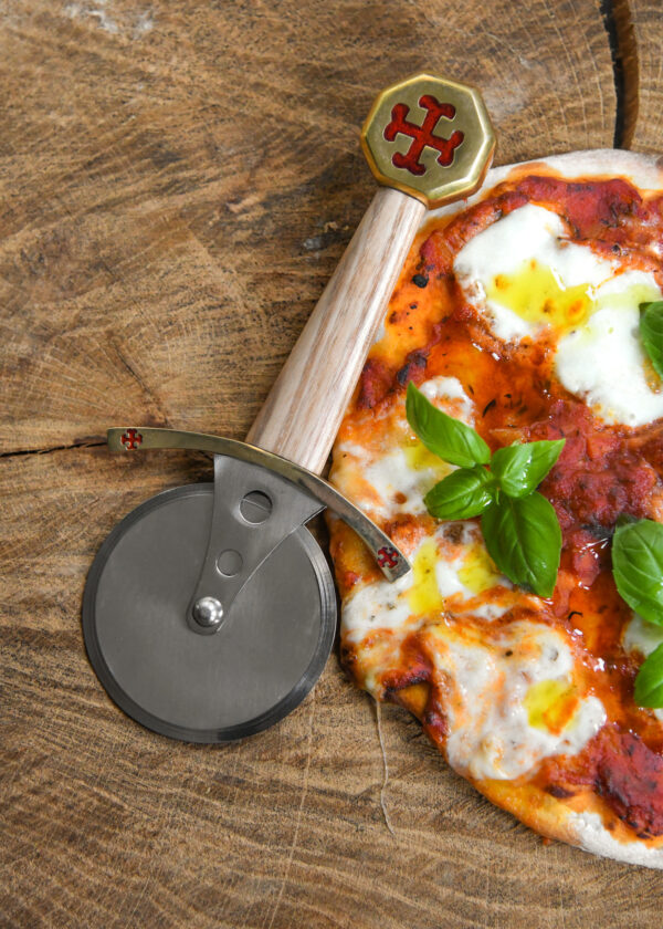 Battle Merchant Pizzaschneider Pizzaroller Templer Schwert Edelstahl, Eschenholz, Messing, Emaille - liegt auf einer Holzscheibe mit einer Pizza Mozarella mit Basilikum