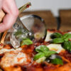 Battle Merchant Pizzaschneider Pizzaroller Templer Schwert Edelstahl, Eschenholz, Messing, Emaille - in einer Hand, die gerade die Pizza Mozarella schneidet