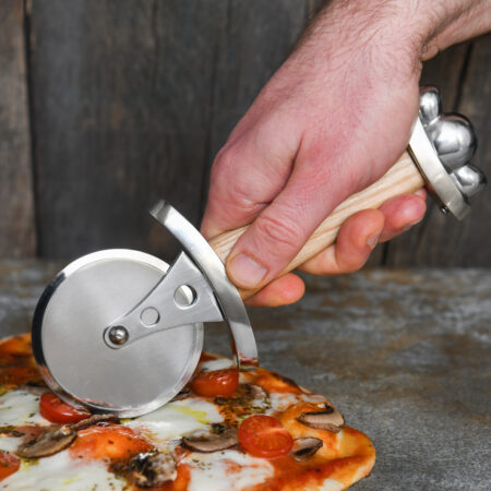 Battle Merchant Pizzaschneider Pizzaroller Wikinger Schwert Edelstahl, Eschenholz, Stahl - Hand hält den Pizzaroller und schneidet eine Pizza auf einem Marmortisch