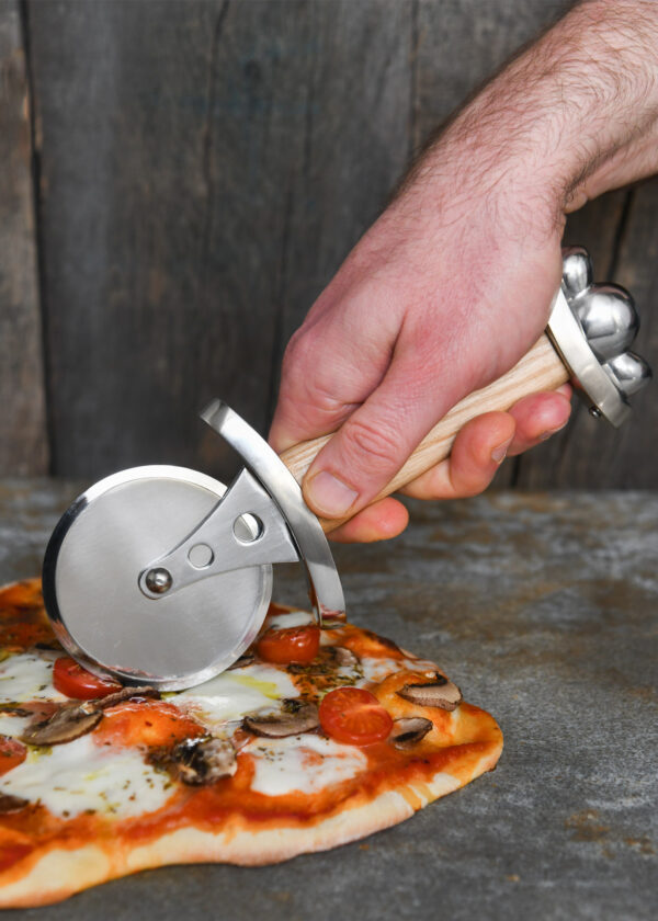 Battle Merchant Pizzaschneider Pizzaroller Wikinger Schwert Edelstahl, Eschenholz, Stahl - Hand hält den Pizzaroller und schneidet eine Pizza auf einem Marmortisch
