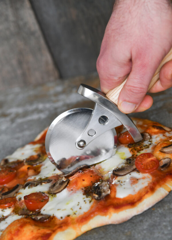 Battle Merchant Pizzaschneider Pizzaroller Wikinger Schwert Edelstahl, Eschenholz, Stahl - Hand hält den Pizzaroller und schneidet eine Pizza auf einem Marmortisch, Ansicht von leicht oben