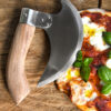 Battle Merchant Pizzaschneider Wiegemesser Wikinger Bartaxt für Pizza und Kräuter Edelstahl, Eschenholz - liegt auf einer Holzscheibe zum Teil auf einer Pizza
