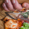 Battle Merchant Pizzaschneider Wiegemesser Wikinger Bartaxt für Pizza und Kräuter Edelstahl, Eschenholz - Hand hält Messer am Griff und schneidet in eine Pizza, Nahaufnahme