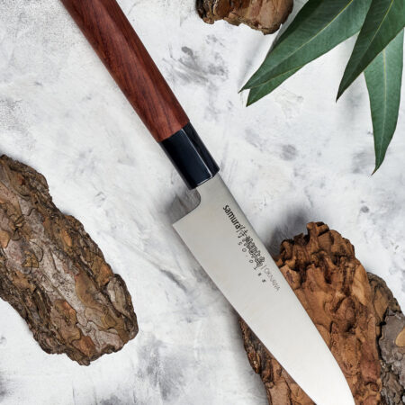 Samura Okinawa Gyuto Küchenmesser 170 mm braun-schwarzer Griff - Messer liegt auf einem Stück Rinde auf einem weiß-grauen Tisch