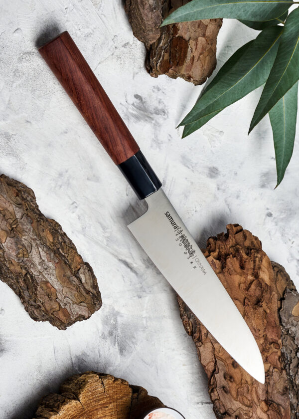 Samura Okinawa Gyuto Küchenmesser 170 mm braun-schwarzer Griff - Messer liegt auf einem Stück Rinde auf einem weiß-grauen Tisch