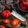 Samura Okinawa Nakiri Küchenmesser 172 mm braun schwarzer Griff - Messer liegt auf einem Brett mit Tomaten und einem Holztisch