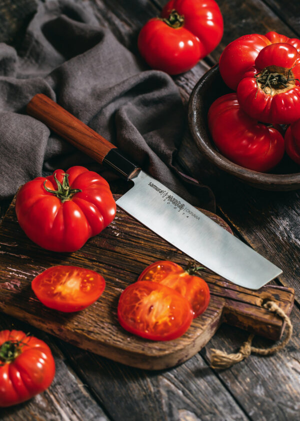Samura Okinawa Nakiri Küchenmesser 172 mm braun schwarzer Griff - Messer liegt auf einem Brett mit Tomaten und einem Holztisch