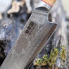 Ha Teikoku Santoku Damaststahl Olivenholz Griff - Nahaufnahme Messer lehnt an ein graues altes Holzstück