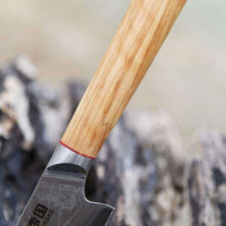 Ha Teikoku Santoku Damaststahl Olivenholz Griff - Nahaufnahme Griff und teil der Klinge, lehnt an ein graues altes Holzstück