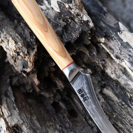 Ha Teikoku Schälmesser Damaststahl - Messer mit der Klinge nach unten rechts auf einem alten grauen Holzstück liegend