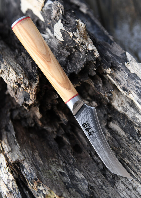 Ha Teikoku Schälmesser Damaststahl - Messer mit der Klinge nach unten rechts auf einem alten grauen Holzstück liegend