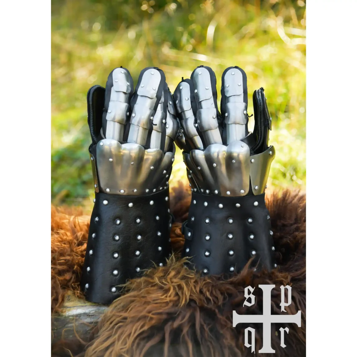 Battle Merchant mittelalterliche Panzerhandschuhe Visby 14. Jh. schwarz - Beide Handschuhe stehend auf dem Gehölz und Fell, Wiese im Hintergrund